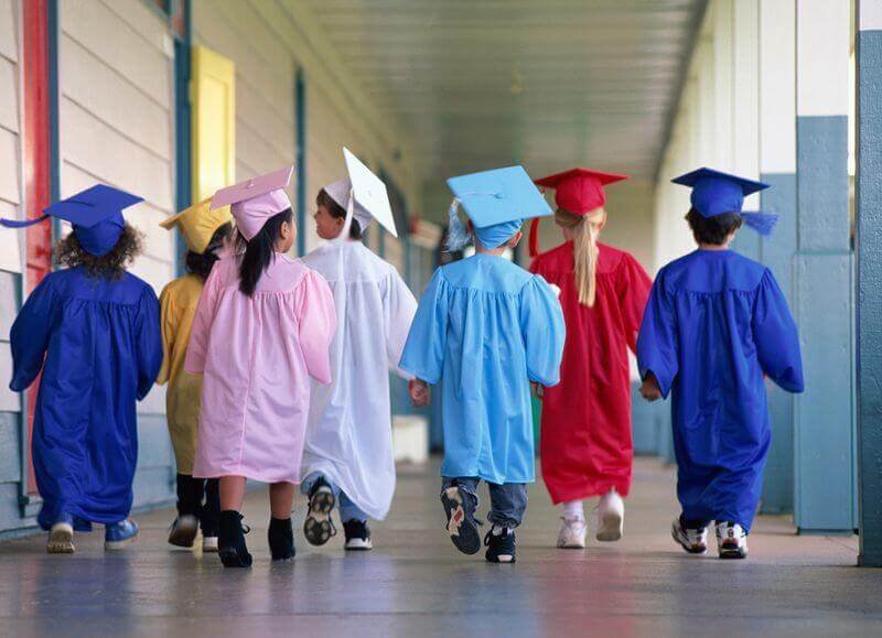 Kids.Graduation.Gowns (3) kids in graduation gowns walking through a outside school hallway